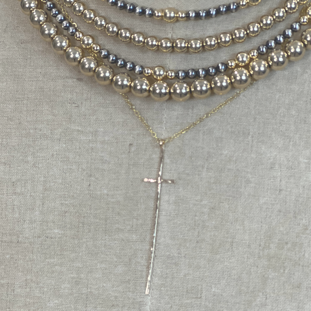 Gold and silver Necklaces with beaded strands and a cross pendant on a textured surface