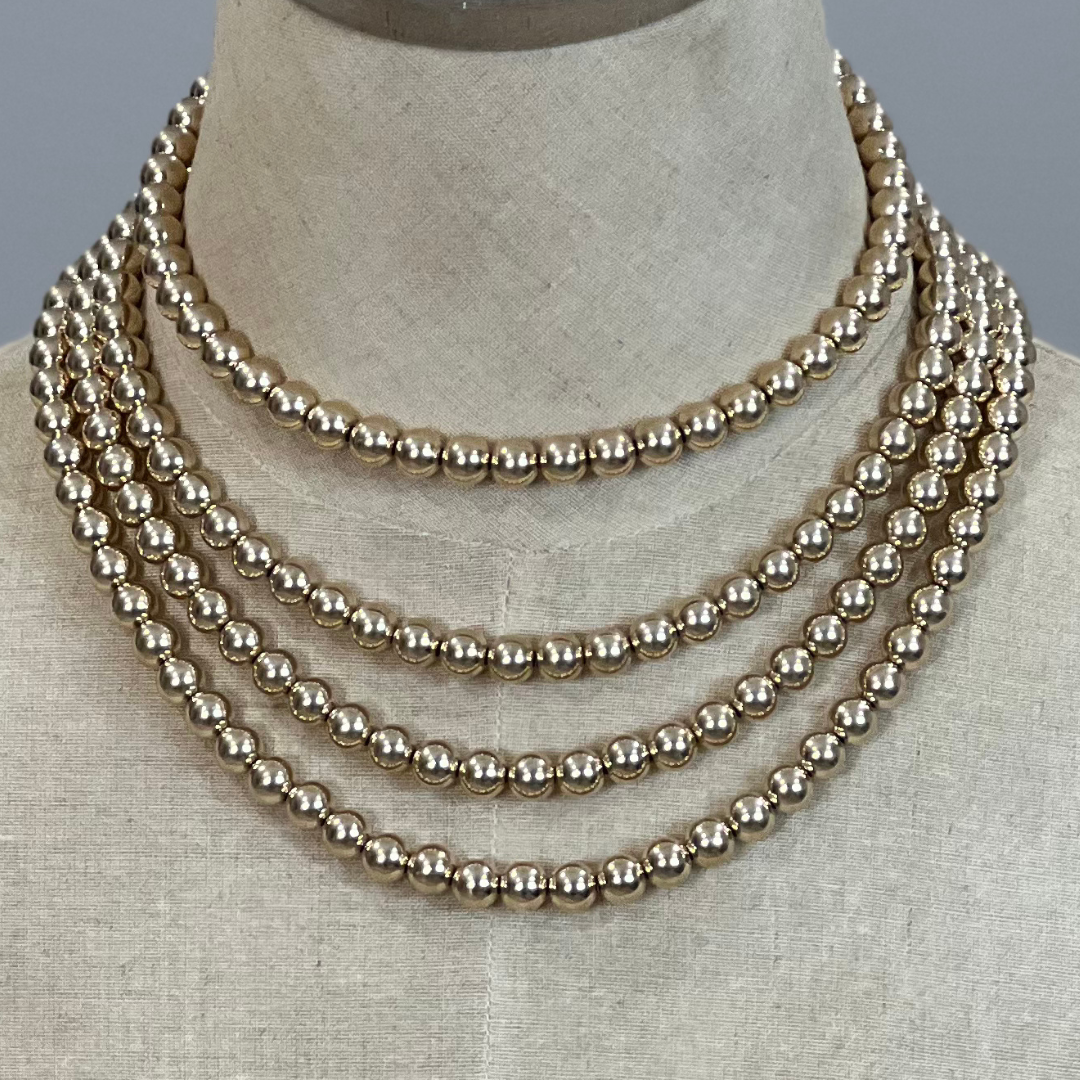 Layered gold pearl bead necklace on a mannequin bust against a neutral background