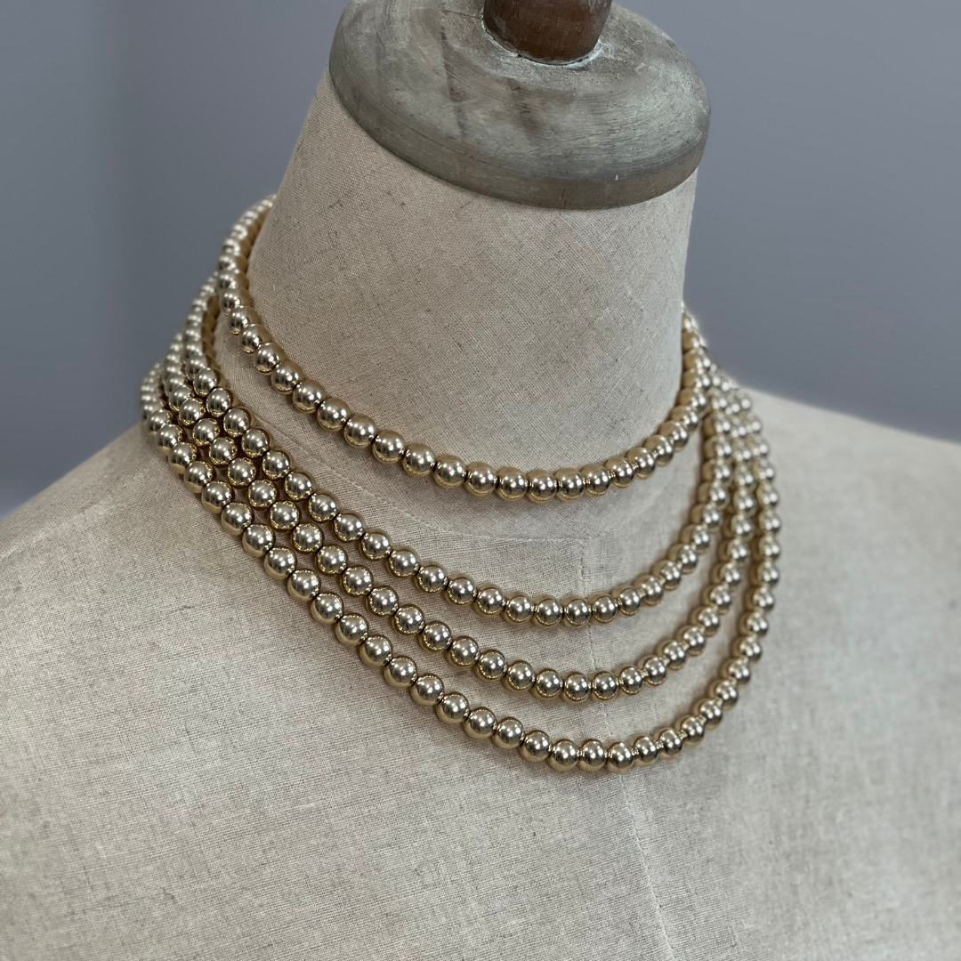 Three gold and silver pearl necklaces on a mannequin bust against a neutral background