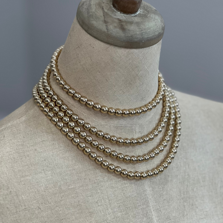 Three gold and silver pearl necklaces on a mannequin bust against a neutral background