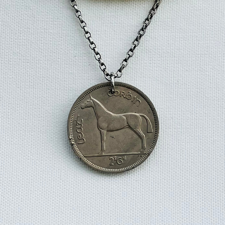 Silver coin pendant with horse design on a chain against a light gray background